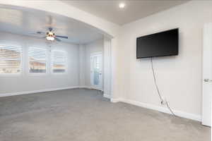 Unfurnished living room featuring ceiling fan, arched walkways, and light carpet