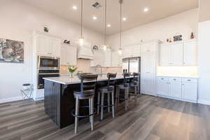 Kitchen with two tone cabinets, a center island with sink, a breakfast bar area, stainless steel appliances, and backsplash