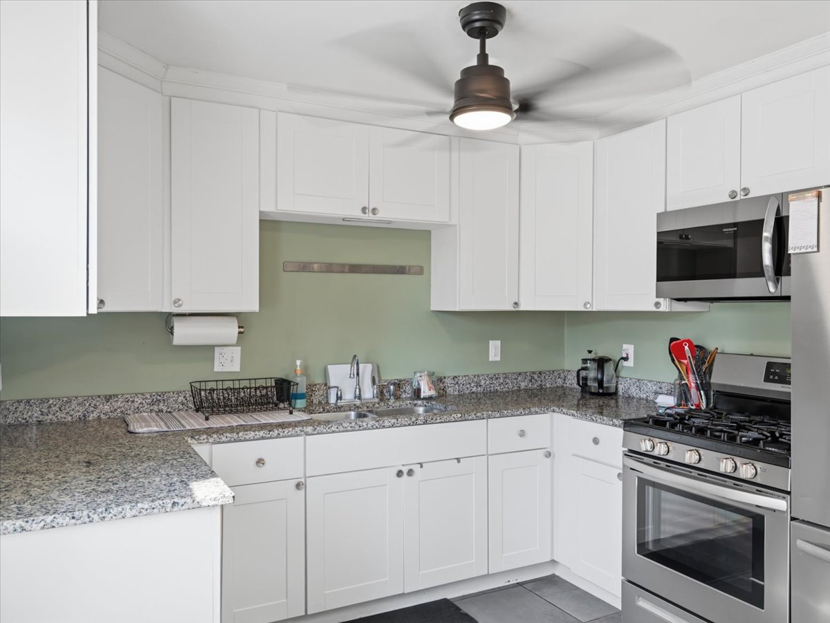 Kitchen with stainless steel appliances, white cabinets, light stone countertops, and ceiling fan