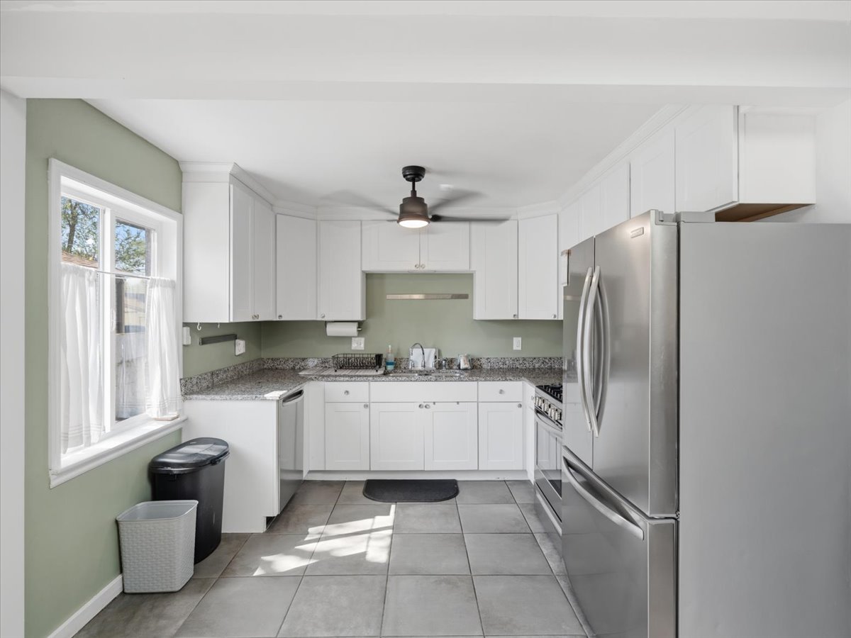 Kitchen featuring stainless steel appliances, white cabinetry, light tile patterned floors, and dark stone counters