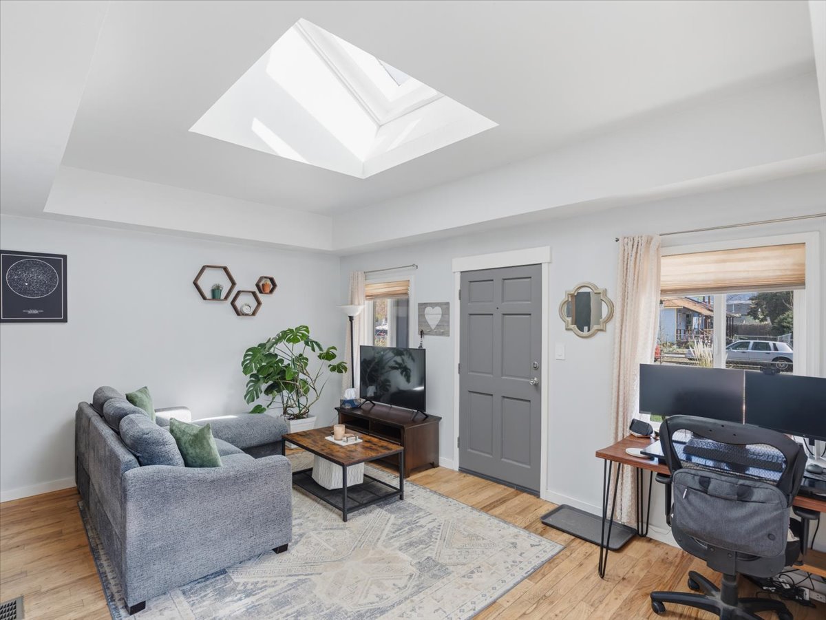 Living area with an office area, a raised ceiling, a skylight, and light wood-style flooring