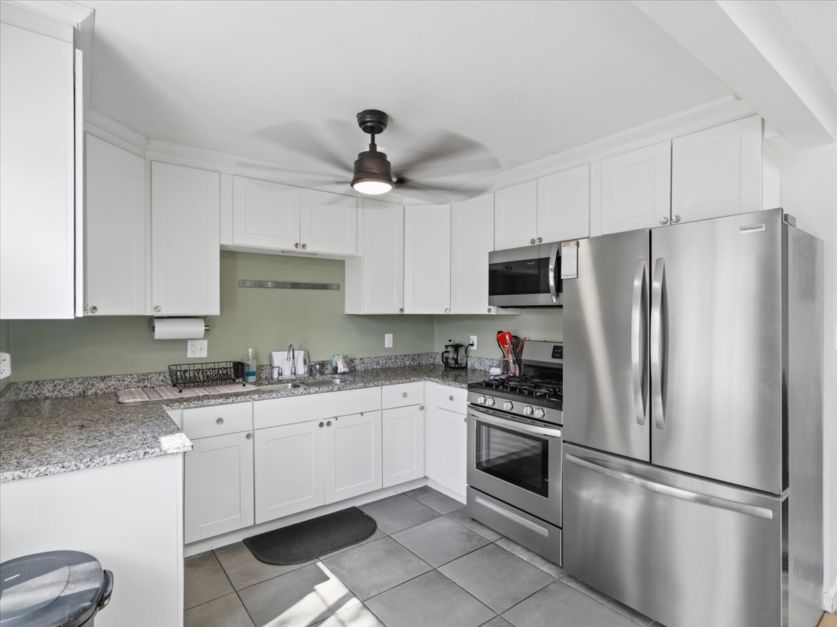 Kitchen featuring stainless steel appliances, white cabinets, light stone counters, ceiling fan, and light tile patterned flooring