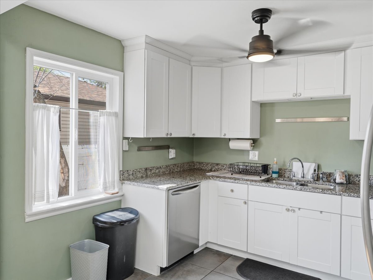 Kitchen with white cabinets, light stone countertops, dishwasher, light tile patterned floors, and a ceiling fan