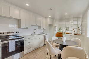 Kitchen featuring stainless steel appliances, white cabinets, light countertops, light wood-type flooring, and decorative backsplash