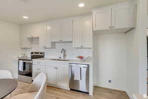 Kitchen featuring stainless steel appliances, white cabinetry, light wood-style flooring, recessed lighting, and backsplash