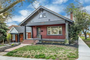 Bungalow-style house with a chimney, covered porch, a front lawn, and brick siding