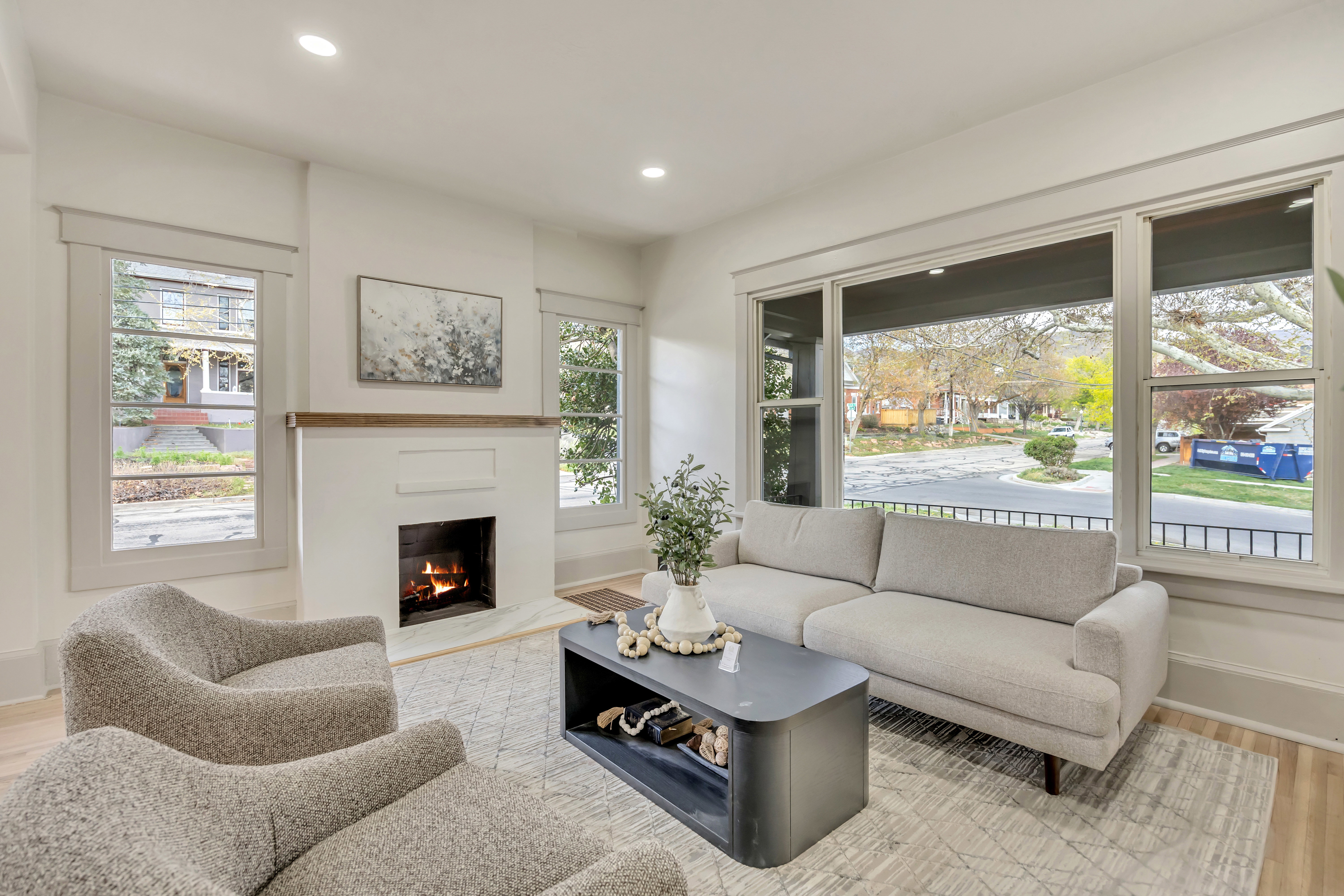 Living room with light wood finished floors, a warm lit fireplace, and recessed lighting