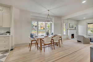 Dining area with light wood-style floors, a warm lit fireplace, and recessed lighting