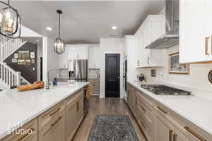 Kitchen featuring hanging lights, stainless steel appliances, dark wood-type flooring, light stone counters, and two tone cabinetry