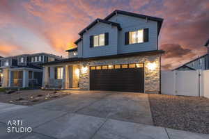 View of front facade with stone siding, a gate, driveway, and an attached garage