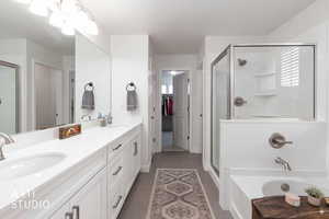 Bathroom with a shower stall, double vanity, dark tile patterned flooring, and a walk in closet