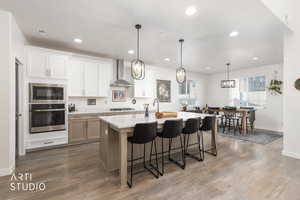 Kitchen with stainless steel appliances, pendant lighting, a breakfast bar, a center island with sink, and light wood-style flooring