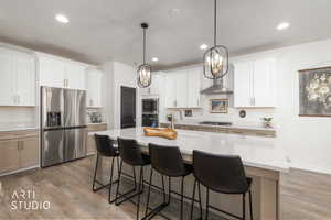 Kitchen featuring a kitchen bar, stainless steel appliances, an island with sink, light stone countertops, and light wood finished floors