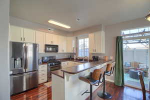Kitchen featuring stainless steel appliances, white cabinets, dark countertops, dark wood-style flooring, and a breakfast bar