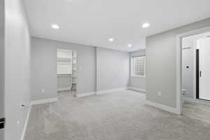 Unfurnished bedroom featuring a walk in closet, recessed lighting, light carpet, and ensuite bathroom