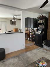 Living room with ceiling fan and wood finished floors looking into dining/kitchen