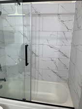 Full bath with a marble finish shower / bath combo