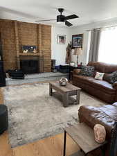Living area with a ceiling fan, wood finished floors, and a fireplace