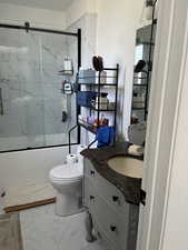 Primary bathroom featuring vanity, light marble finish floors, and bath / shower combo with glass door