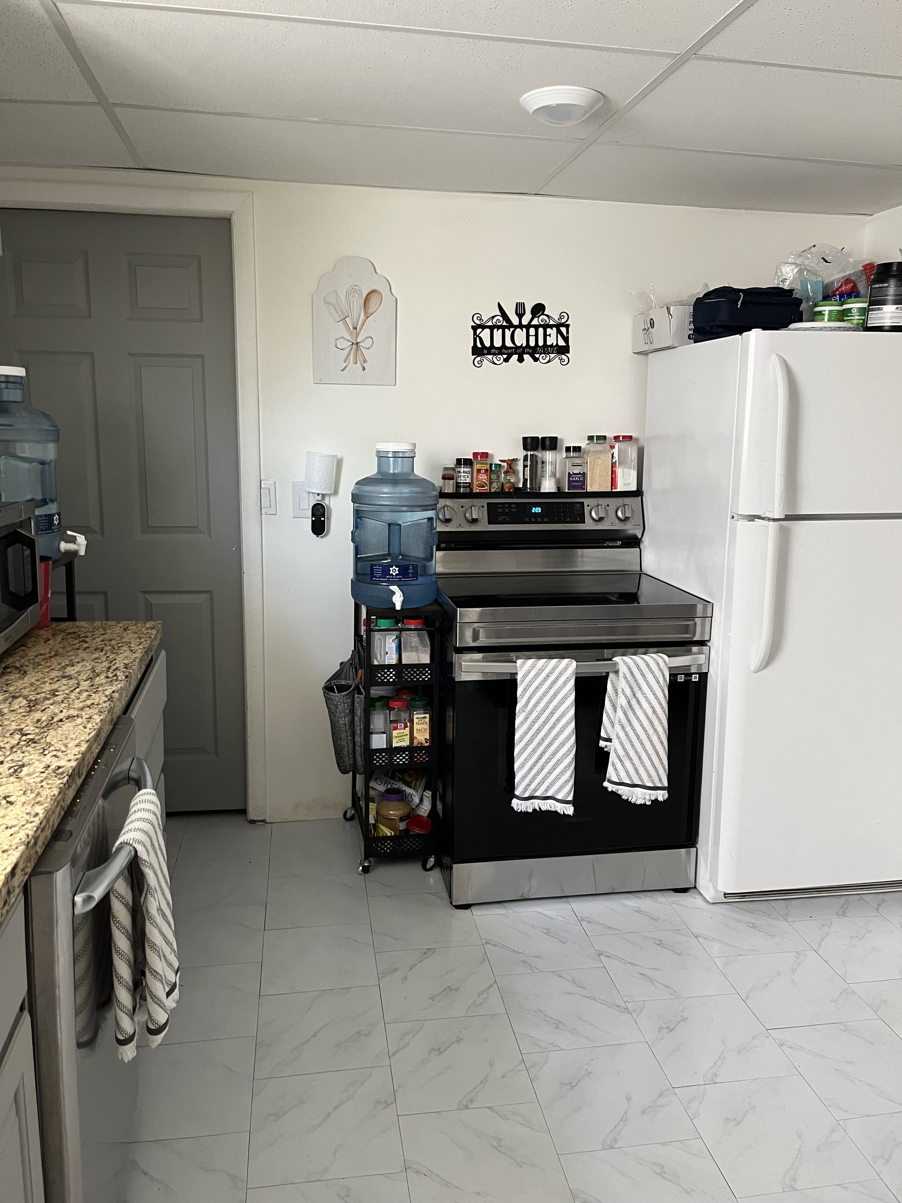 Kitchen featuring stainless steel appliances, a drop ceiling, light marble finish flooring, and light stone countertops