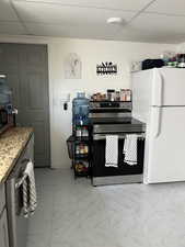 Kitchen featuring stainless steel appliances, a drop ceiling, light marble finish flooring, and light stone countertops