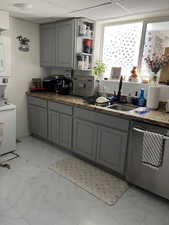 Kitchen featuring gray cabinets, light marble finish flooring, washer and drier with above ground window looking into back yard