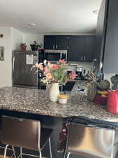 Kitchen with stainless steel appliances, granite counters, a breakfast bar, and dark cabinets