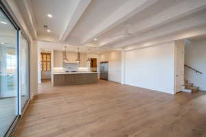 Kitchen featuring beamed ceiling, light countertops, hanging light fixtures, light wood-style flooring, and a large island with sink