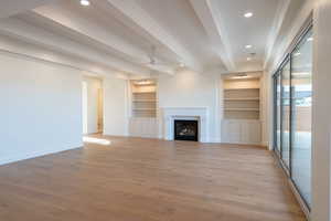 Unfurnished living room with built in shelves, beam ceiling, light wood-type flooring, a ceiling fan, and a fireplace