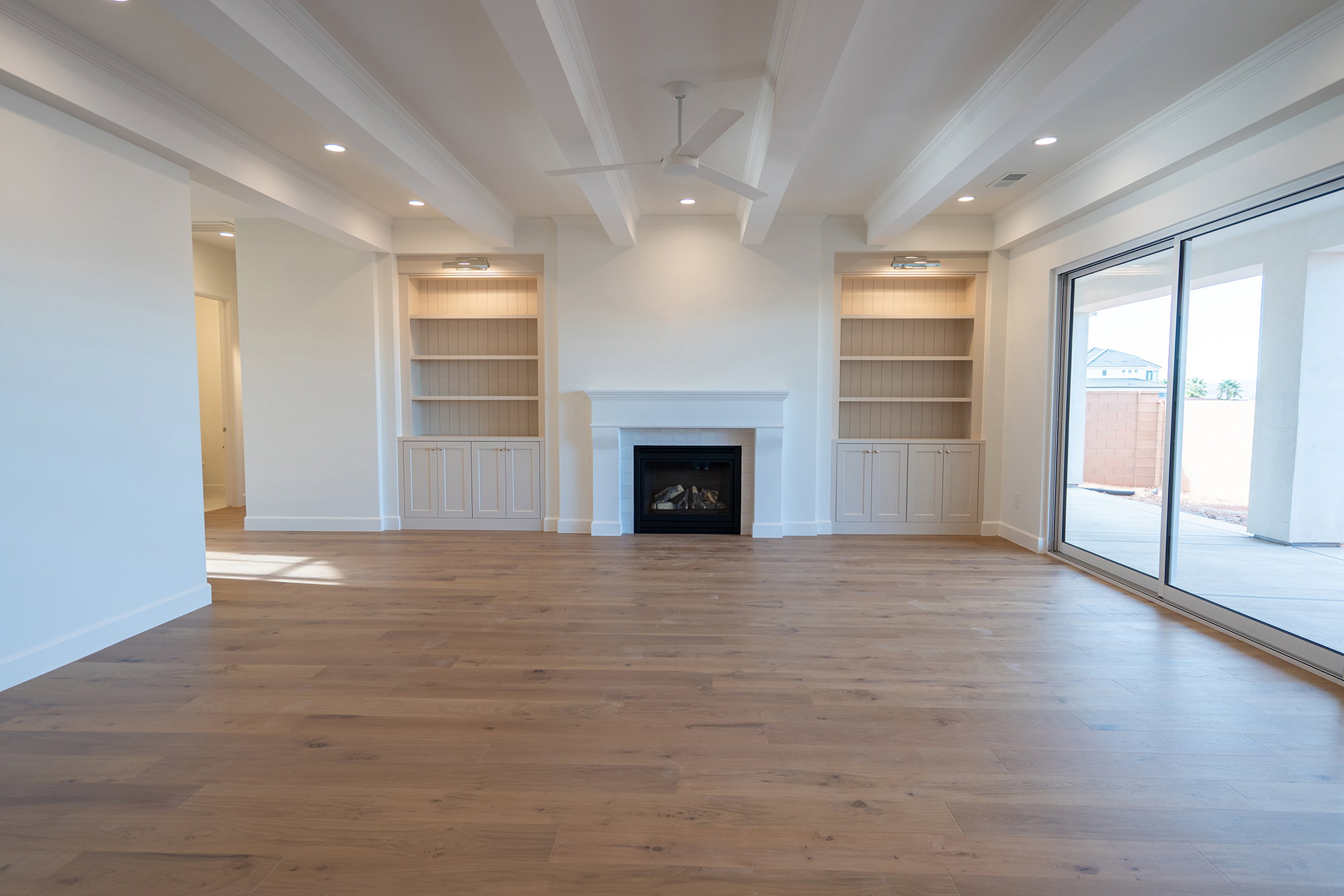 Unfurnished living room featuring built in shelves, beam ceiling, ceiling fan, light wood-style flooring, and a fireplace