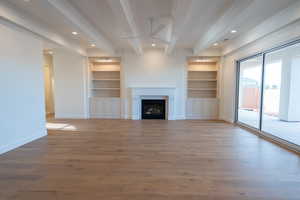 Unfurnished living room featuring built in shelves, beam ceiling, ceiling fan, light wood-style flooring, and a fireplace