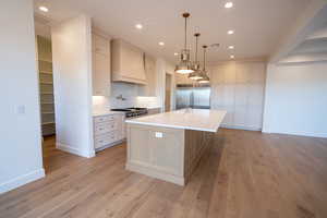 Two tone kitchen with stainless steel appliances, a kitchen island with sink, light wood-style flooring, decorative backsplash, and light stone countertops