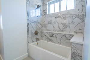 Bathroom featuring a combined bath / shower with marble appearance and baseboards
