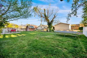 Fenced backyard featuring a trampoline, a residential view, and a storage unit