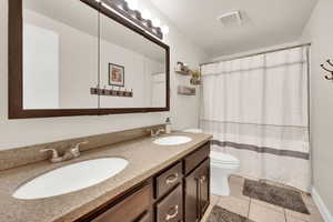 Bathroom with double vanity, light tile patterned floors, and shower / bath combo with shower curtain