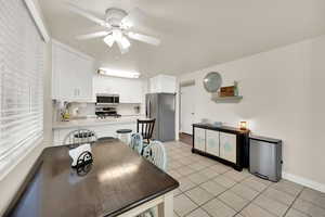 Kitchen with light countertops, stainless steel appliances, white cabinets, a ceiling fan, and light tile patterned floors