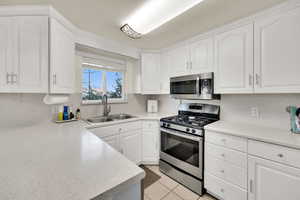 Kitchen with stainless steel appliances, white cabinets, light countertops, and light tile patterned floors