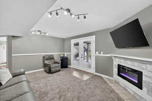 Living room with french doors, light tile patterned floors, a fireplace with flush hearth, a textured ceiling, and track lighting