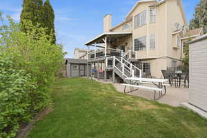 Rear view of house featuring a patio area, a lawn, a chimney, outdoor dining area, and a storage shed