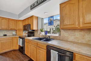 Kitchen featuring black / electric stove, tile countertops, dishwashing machine, dark wood-style floors, and decorative backsplash