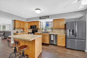 Kitchen featuring stainless steel appliances, tile countertops, light wood finished floors, a kitchen island, and decorative backsplash