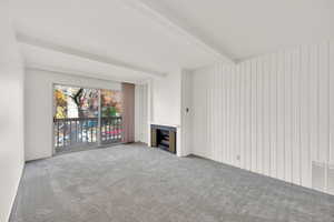 Unfurnished living room featuring carpet flooring, a fireplace, beam ceiling, and wood walls