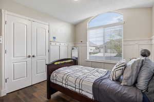 Bedroom featuring a wainscoted wall, dark wood-style flooring, a decorative wall, and a closet