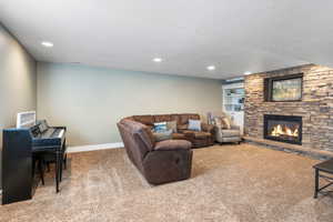 Living area with built in features, a textured ceiling, carpet flooring, a stone fireplace, and recessed lighting