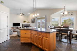 Kitchen with vaulted ceiling, stone tile flooring, a tile fireplace, plenty of natural light, and a center island