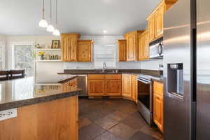 Kitchen with stainless steel appliances, open shelves, hanging light fixtures, stone tile flooring, and plenty of natural light