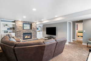 Living area featuring built in shelves, light carpet, a stone fireplace, a textured ceiling, and recessed lighting