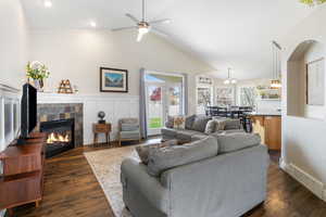 Living area with dark wood-style flooring, a fireplace, a ceiling fan, lofted ceiling, and wainscoting