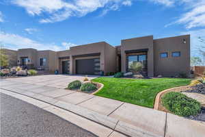 Adobe home with an attached garage, a front yard, stucco siding, driveway, and stone siding