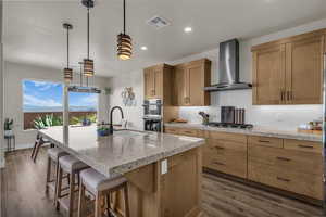 Kitchen featuring tasteful backsplash, dark wood-style flooring, a breakfast bar, a kitchen island with sink, and light stone countertops
